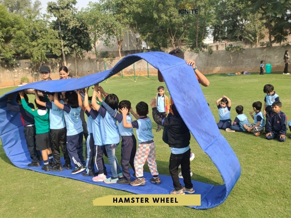 Students inside a large blue fabric 'hamster wheel' being guided by instructors