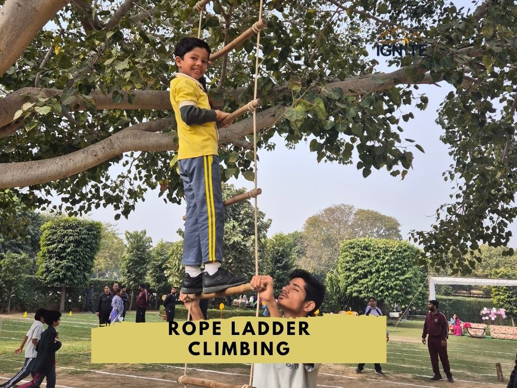 A young boy climbing a rope ladder, with an instructor assisting from below