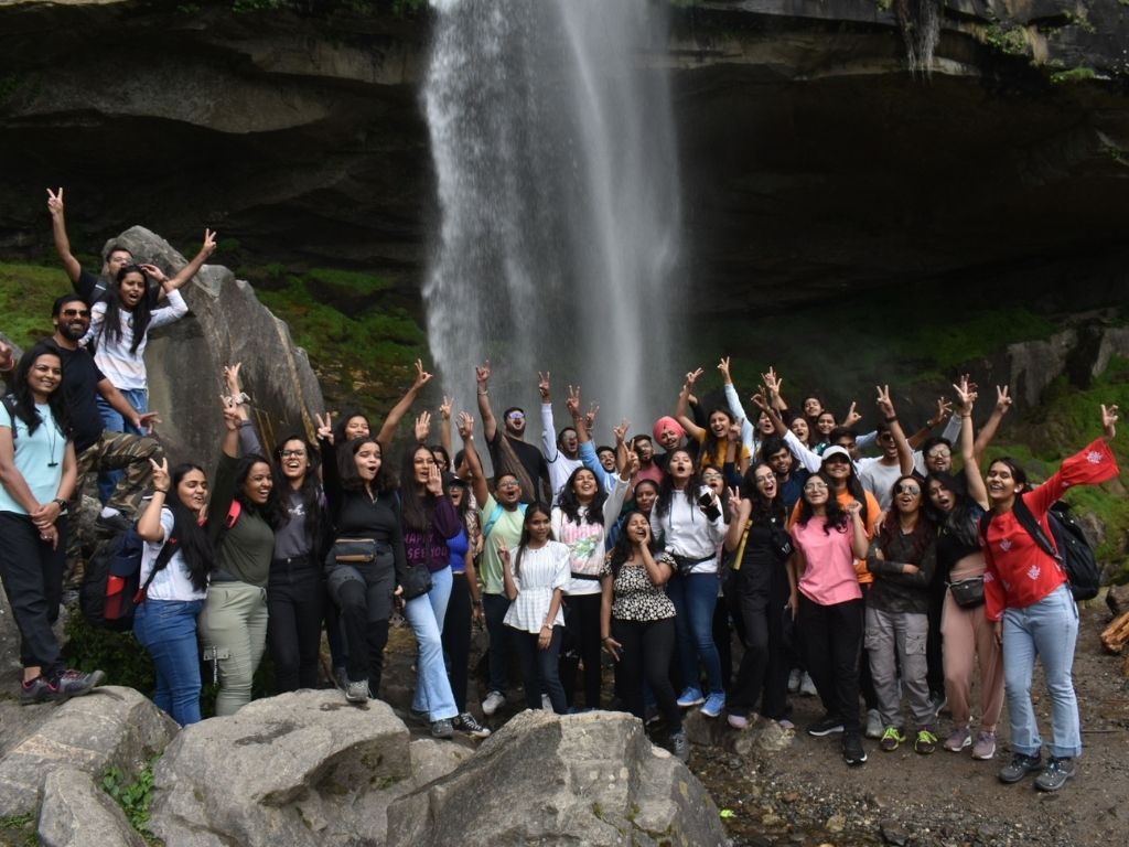 Group of people posing excitedly in front of a waterfall